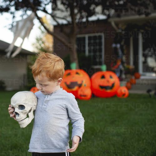 toddler-holding-skeleton-head-in-front-of-outdoor-halloween-decor-CAVF86707